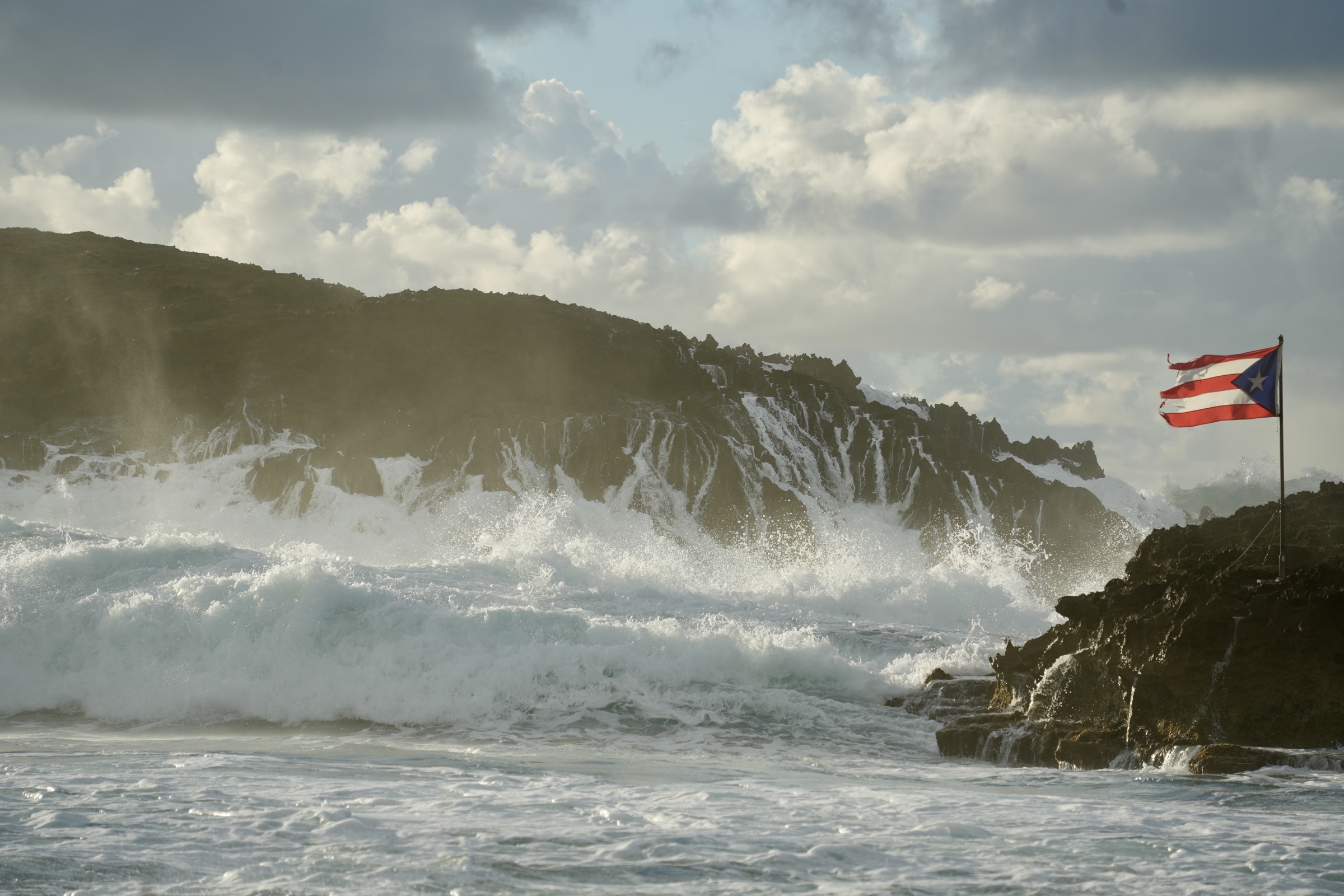 Waves breaking beside a Puerto Rican flag on a rocky coast