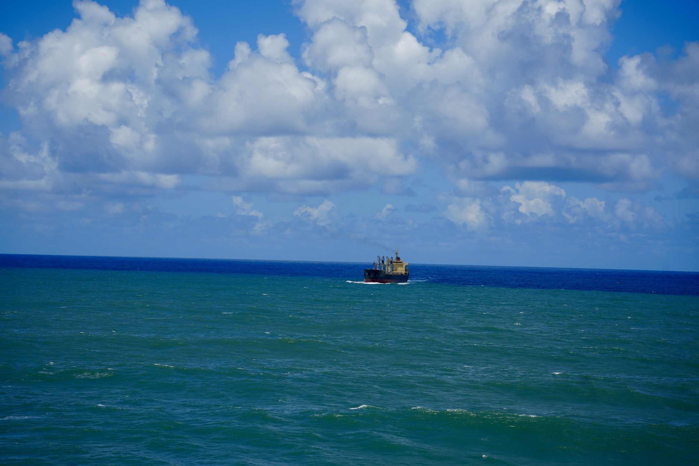 A solitary cargo ship crossing a blue horizon